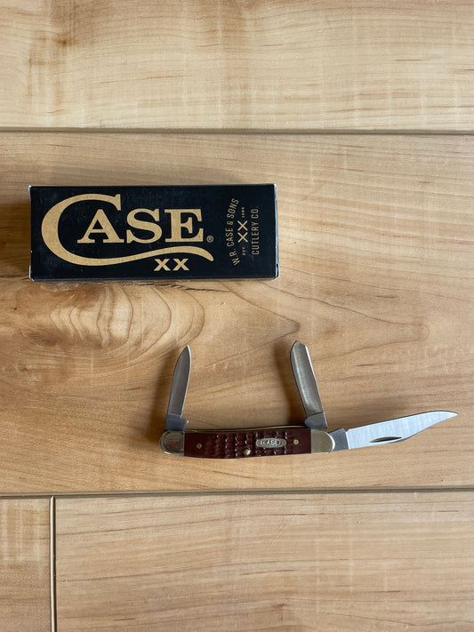 A stainless steel hunting knife with a brown jigged Delrin handle and nickel silver bolster, displayed in front of its brown cardboard box with 'CASE' and 'X' branding.