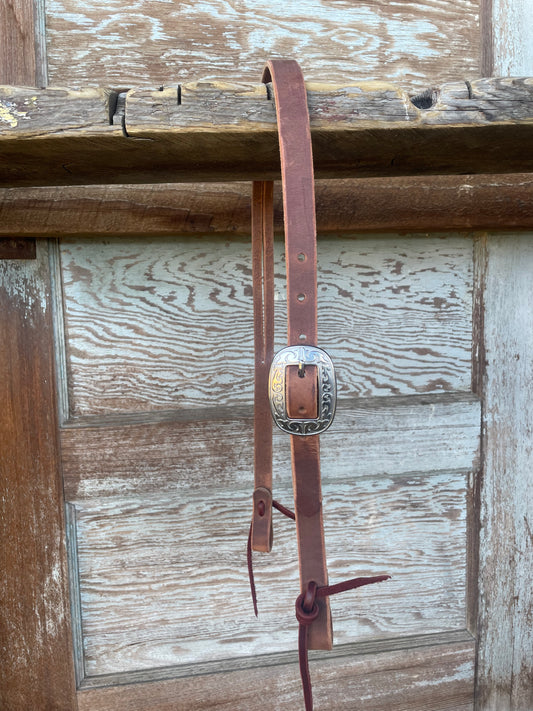 A brown leather slit ear headstall with stainless steel buckles, displayed against a wooden background.