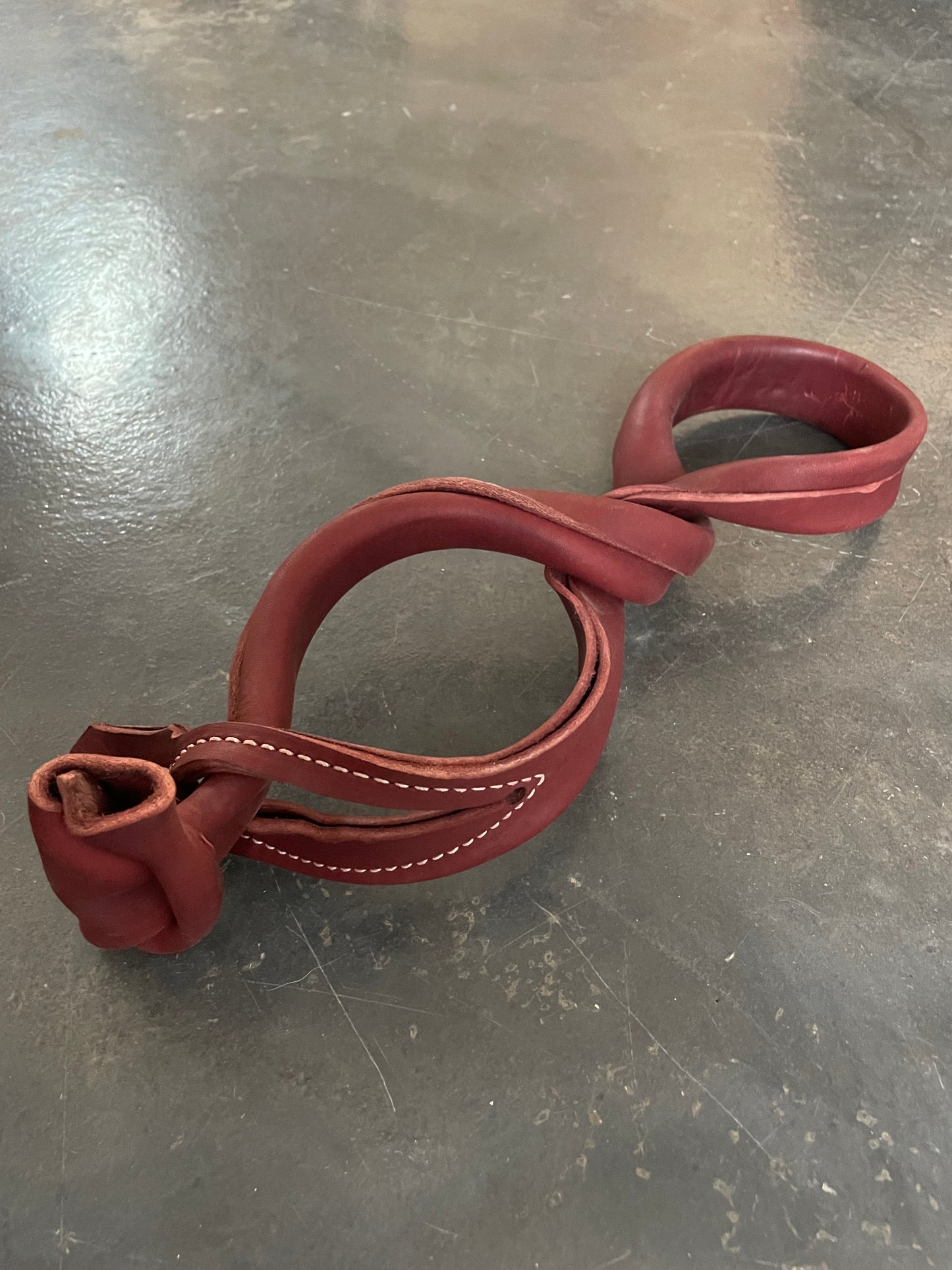 A pair of red leather horse hobbles on a gray floor.