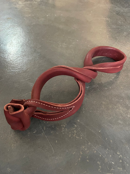 A pair of red leather horse hobbles on a gray floor.