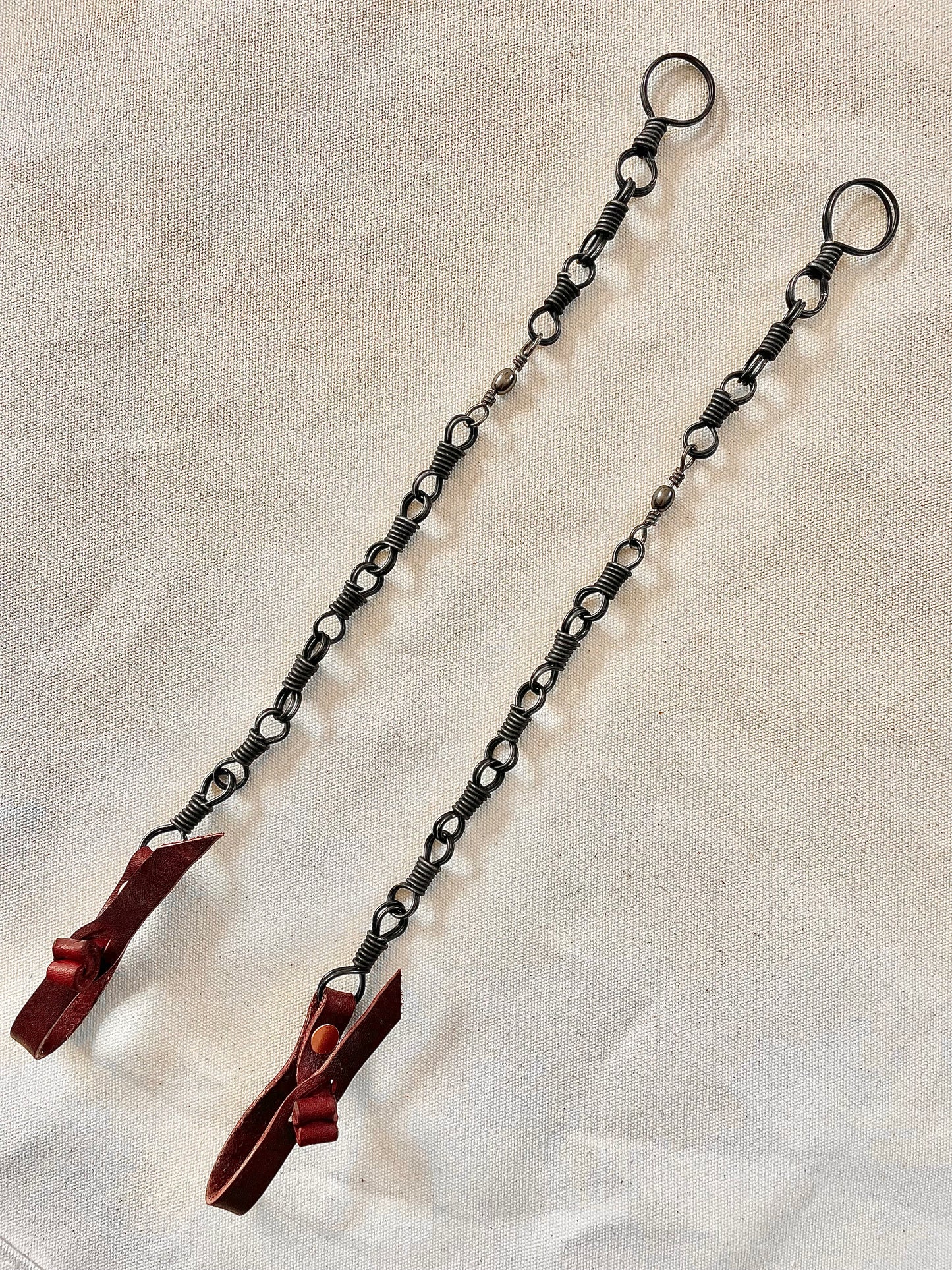 Two metal chains with looped ends and red attachments laid out on a beige surface.