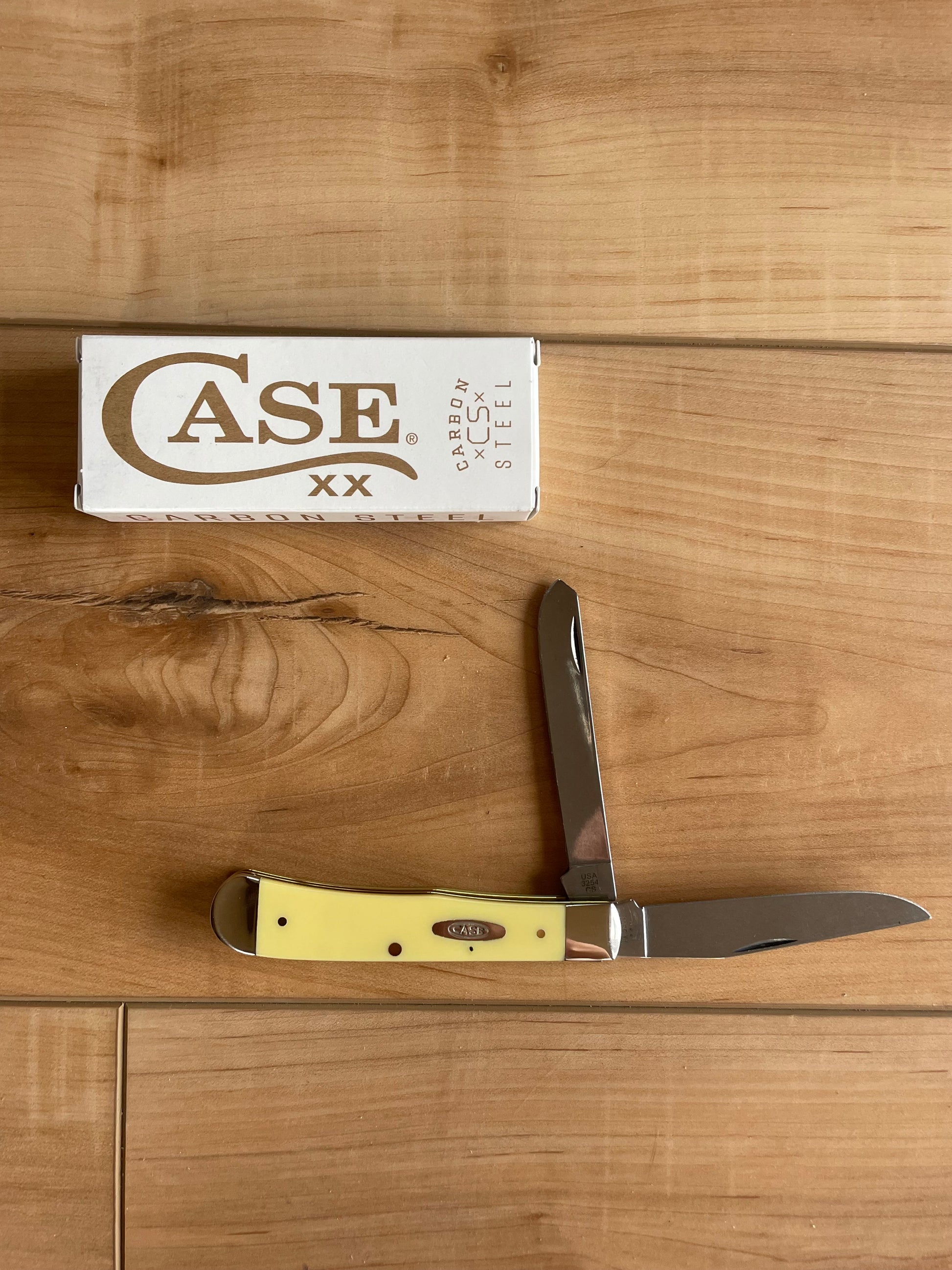 A yellow carbon steel knife with a smooth synthetic handle and nickel silver bolster, displayed in front of its cardboard packaging labeled 'CASE'.