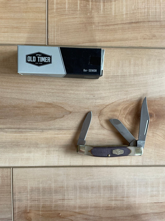A folding knife with a stainless steel blade and a wooden handle with a nickel silver bolster and inlay shield, featuring the Old Timer brand logo.