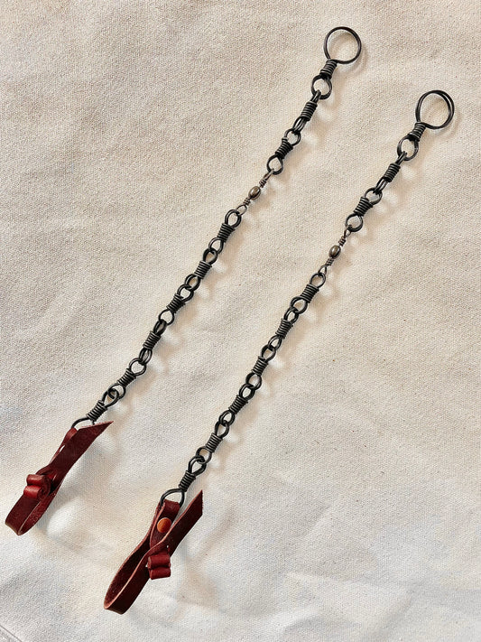 Two metal chains with looped ends and red attachments laid out on a beige surface.