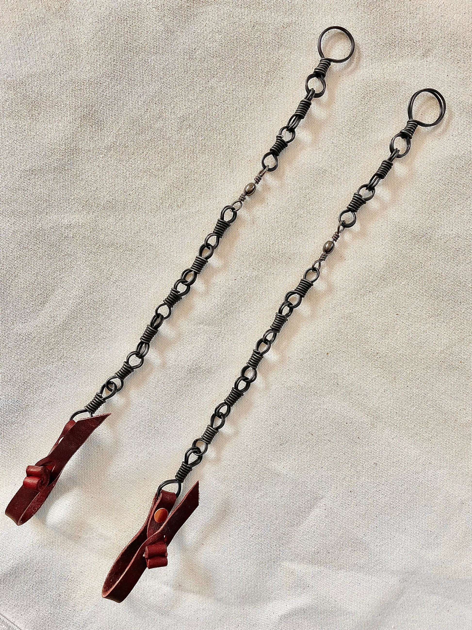 Two metal chains with looped ends and red attachments laid out on a beige surface.